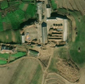 6/6 Cour de ferme (landuse=farmyard) composée de longs bâtiments parsemée des tas de foins. Cimetière désordonné en bas à droite de l'image (voir la section sur les cimetières pour plus de détail) (imagerie satellite Maxar).