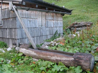wooden trough fed by water from the rain gutter of a hut