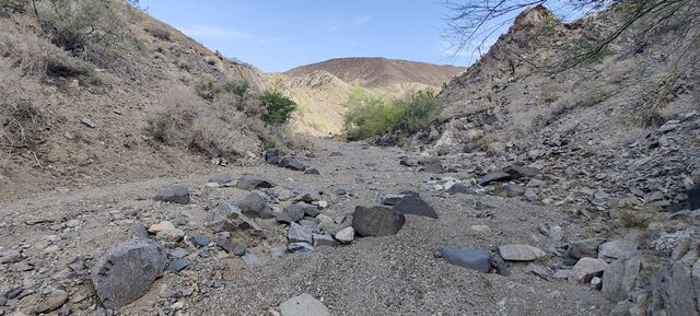 A photo of a narrow wadi containing mixed material ranging in size from sand to boulders.